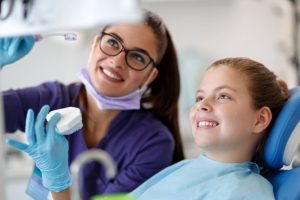 Smiling young girl seated with orthodontics assistant