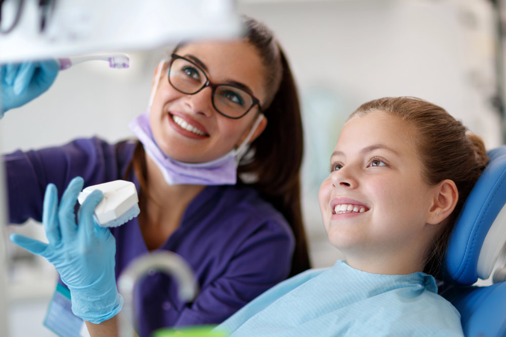 Smiling young girl seated with orthodontics assistant