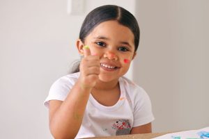 Smiling young girl fingerpainting with thumbs up