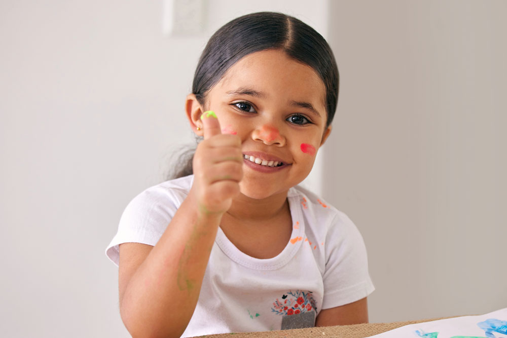 Smiling young girl fingerpainting with thumbs up
